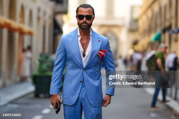 Guest wears black sunglasses, a khaki cordon with silver pendant necklace, a white shirt, a blue with red buttoned blazer jacket, matching blue suit...