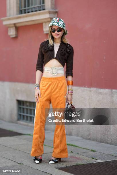 Guest wears a dark green with white embroidered flower pattern bob hat from Carhartt, brown marble print pattern sunglasses, green stones earrings, a...