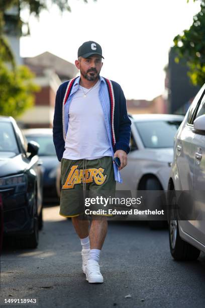 Guest wears a gray with white C logo embroidered pattern cap, a gold chain pendant necklace, a white t-shirt, a pale blue with white striped print...