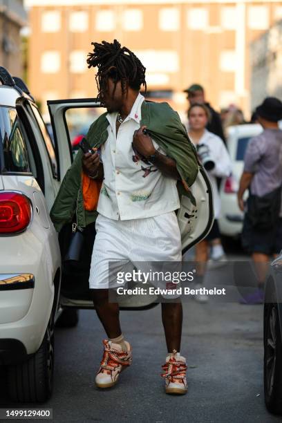 Guest wears white pearls necklaces, a white shirt, a khaki with orange interior zipper bomber coat, white ribbed sport shorts from Supreme, beige...