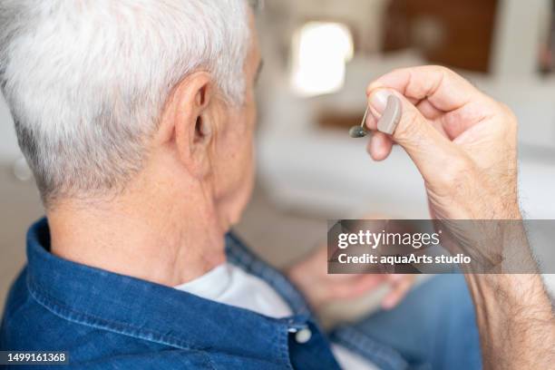 senior man placing hearing aid on his ear - ear drum stock pictures, royalty-free photos & images