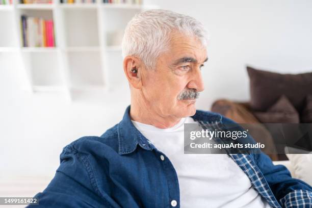 älterer mann mit hörgerät zu hause - hineinstecken stock-fotos und bilder