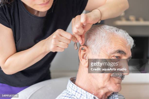 caregiver helping senior man with hearing aid - ear exam stock pictures, royalty-free photos & images