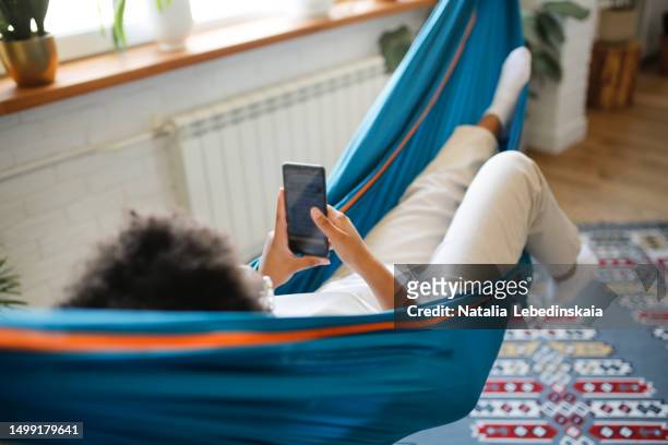 tranquil retreat: serene mixed race teenage kid girl with smartphone resting in hammock at home - smartphones dangling stock pictures, royalty-free photos & images