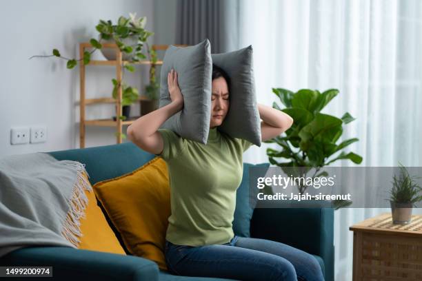 asian woman feel boring have a problems with noise covering ears with pillows sitting at home. - buren stockfoto's en -beelden