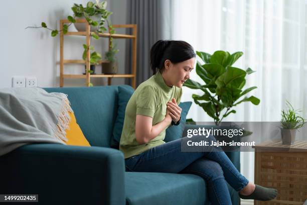 asiatische frau mit brustschmerzen sitzt auf dem sofa im wohnzimmer zu hause. - reflux stock-fotos und bilder