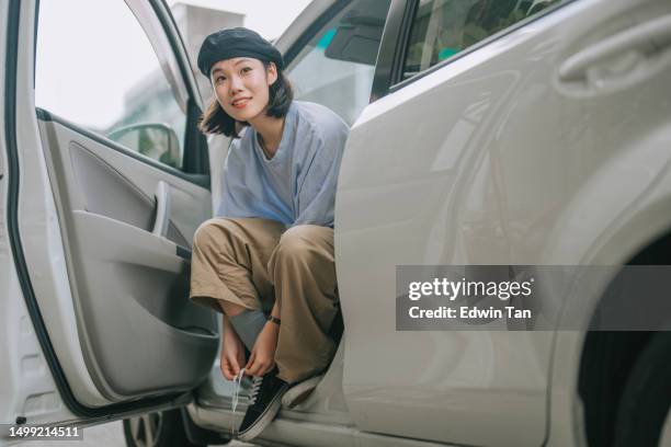 asian chinese young woman tying shoelace in passenger seat smiling at roadside - malaysian people stock pictures, royalty-free photos & images
