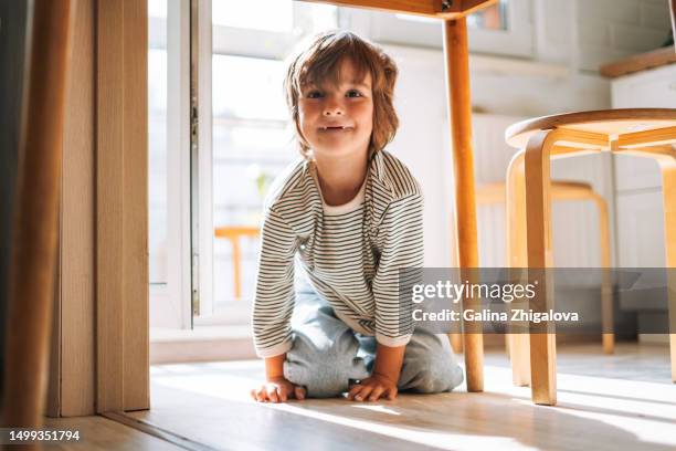 funny child boy 4-5 years old sitting and having fun under table in kitchen at home - 4 5 years stock pictures, royalty-free photos & images