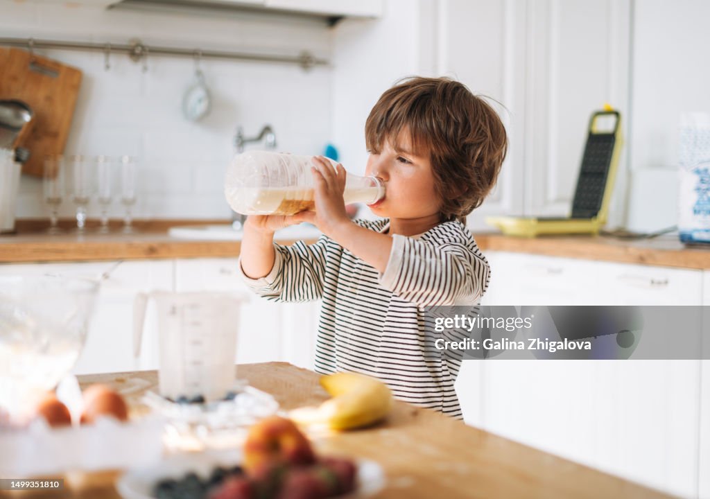 Cute small child boy 4-5 years cooking and drink milk in kitchen at home