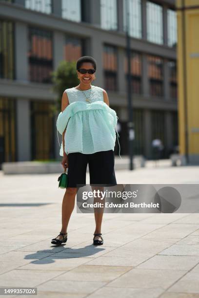 Tamu McPherson wears brown marble print pattern sunglasses, gold earrings, a transparent / red / yellow / green pearls with a large T pendant long...