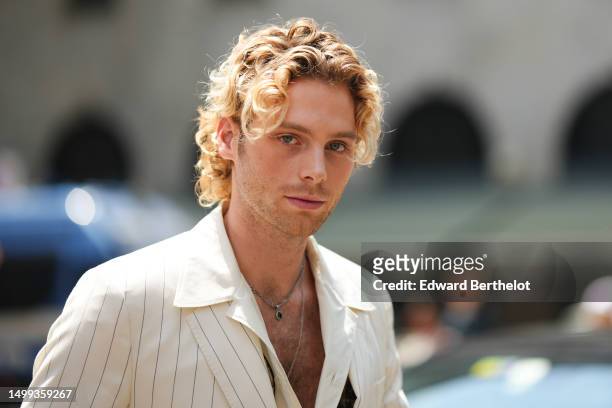 Luke Hemmings wears silver chain pendant necklaces, a pale yellow striped print pattern blazer jacket, a pale yellow shirt, outside Dolce & Gabbana,...