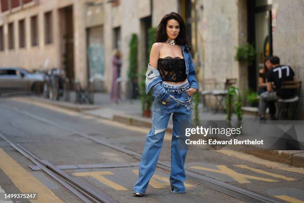 Guest wears a silver large logo necklace from Dolce & Gabbana, a black lace print pattern shoulder-off / corset top, a blue denim buttoned jacket,...