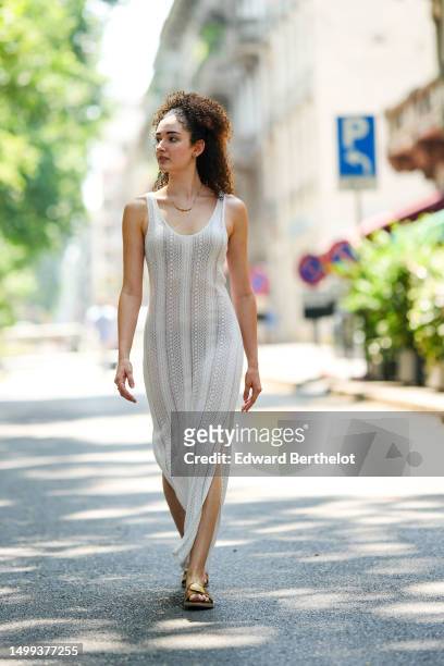 Guest wears gold earrings, a gold chain with beige pearls necklace, a white cut-out pattern wool sleeveless long slit / split dress, brown camel...