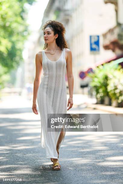 Guest wears gold earrings, a gold chain with beige pearls necklace, a white cut-out pattern wool sleeveless long slit / split dress, brown camel...