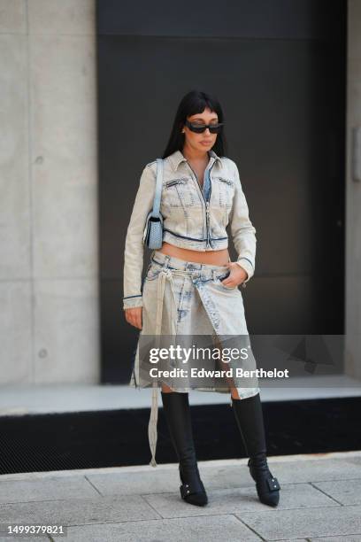 Guest wears black sunglasses, silver small earrings, a blue faded denim zipper cropped jacket, a matching blue faded denim slit / split pleated knees...