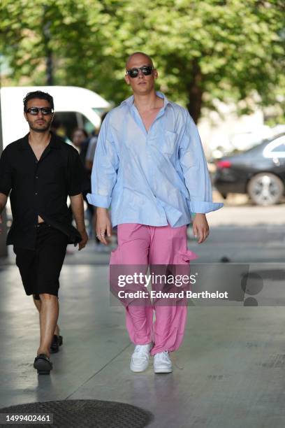 Guest wears black sunglasses, a pale blue oversized shirt, pink large cargo pants, white leather sneakers , outside Neil Barrett, during the Milan...