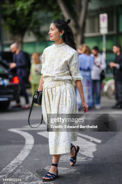 Guest wears green earrings, a white with black small print pattern long sleeves / ripped blouse, a matching white with black small print pattern...