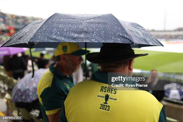 Australian fans shelter from the rain under an umbrella as the covers come on during a rain delay on Day Three of the LV= Insurance Ashes 1st Test...