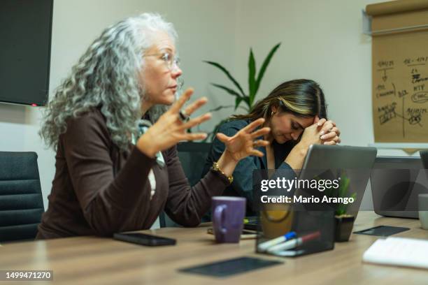 frustrierte millennial-arbeitnehmerin, die mit kollegen am tisch sitzt - kommunikationsproblem stock-fotos und bilder