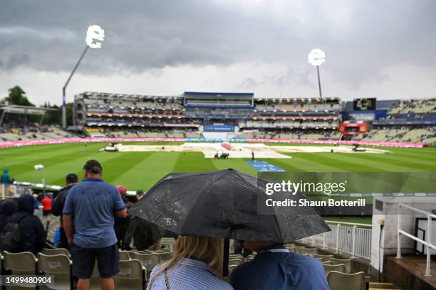 Spectators shelter from the rain under an umbrella as the covers come on during a rain delay on Day Three of the LV= Insurance Ashes 1st Test match...