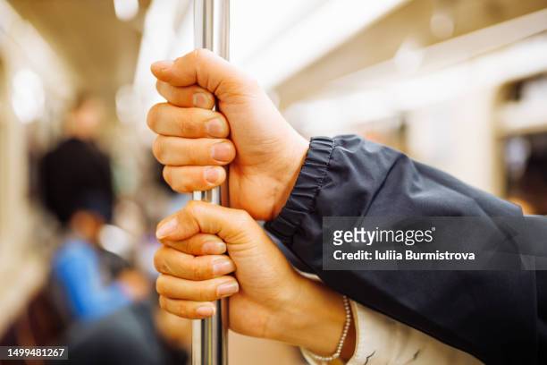 hands of unrecognizable mature people wearing jackets holding onto metal handrail in subway car - metro st petersburg stockfoto's en -beelden