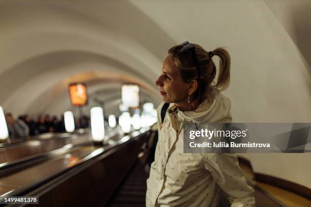 cheerful woman with ponytail wearing white jacket riding escalator at subway station - metro st petersburg stockfoto's en -beelden