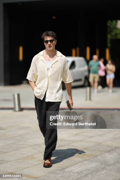 Guest wears black sunglasses, a white tank-top, a white latte mesh / fishnet buttoned polo shirt, black linen suit pants, camel shiny leather and...