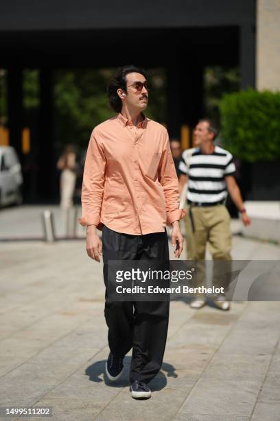 Guest wears black sunglasses, a pale orange shirt, black large suit pants, navy blue denim sneakers , outside Neil Barrett, during the Milan Fashion...