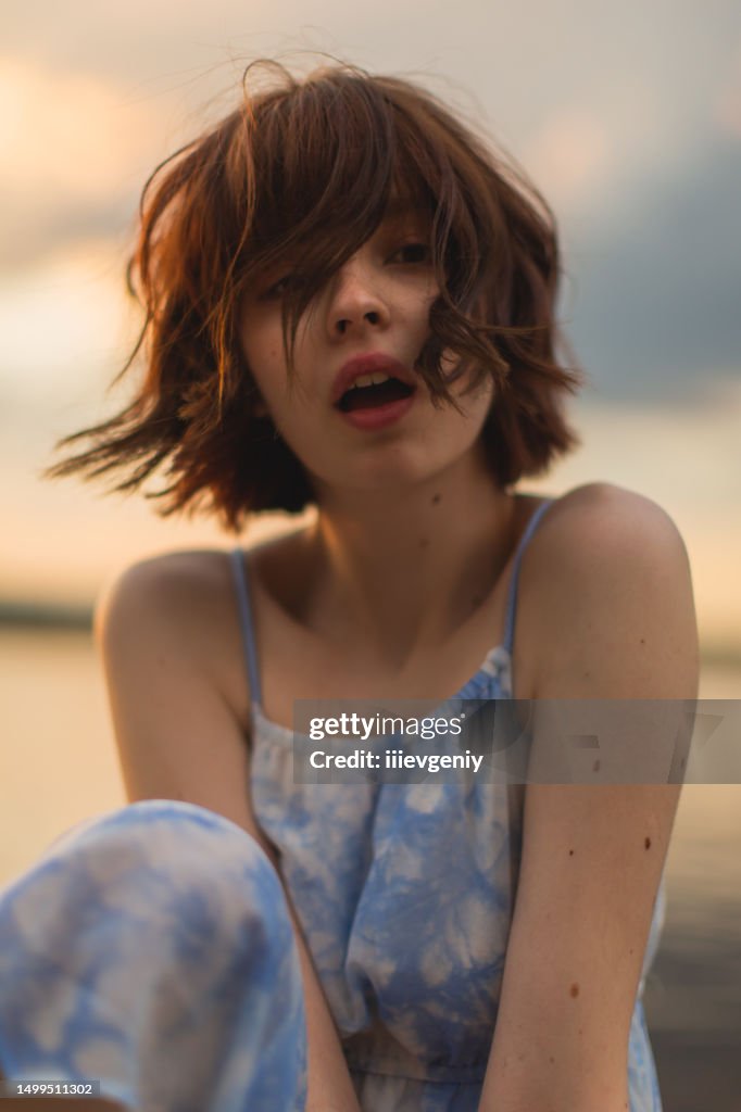 Asian woman in dress on sunset sky background. Bobbed hair. Summer. Mole on skin. Beauty portrait