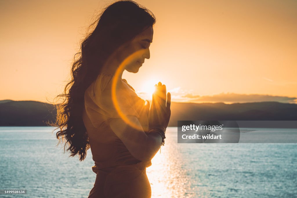 Beautiful girl is meditating , doing yoga prayer pose during sunset in Lake Salda in Burdur , Turkey