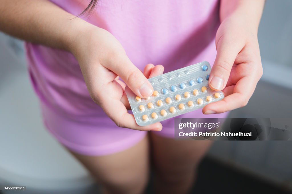 Unrecognizable Young Woman, Wearing a Pink Pajama, holding her Birth Control Pills While Standing in the Bathroom
