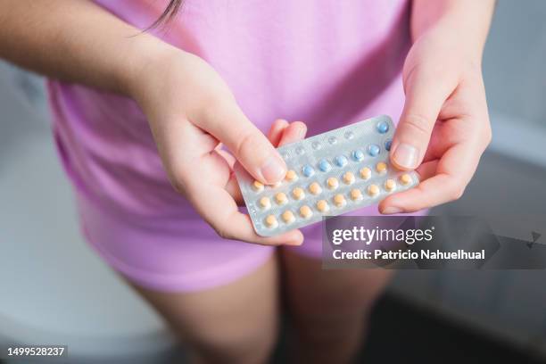 unrecognizable young woman, wearing a pink pajama, holding her birth control pills while standing in the bathroom - contraceptive pill stock pictures, royalty-free photos & images