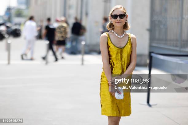 Jenny Walton is seen wearing brown sunglasses, pearl earrings, a pearl necklace, gold sandals, a white mini bag embroidered with beads and a gold...