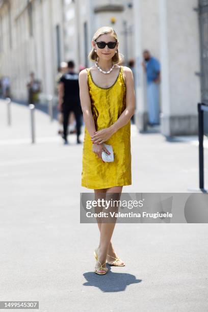 Jenny Walton is seen wearing brown sunglasses, pearl earrings, a pearl necklace, gold sandals, a white mini bag embroidered with beads and a gold...