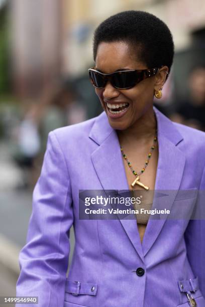 Tamu McPherson is seen wearing brown sunglasses, gold hoop earrings, a long colorful necklace, a beige bra top and a violet suit jacket outside JW...