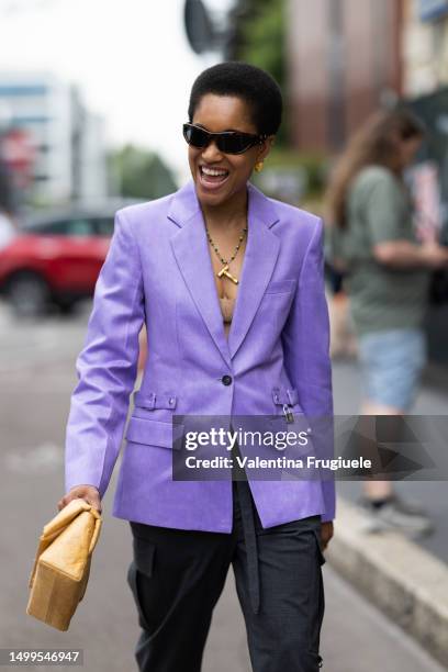 Tamu McPherson is seen wearing brown sunglasses, gold hoop earrings, a long colorful necklace, a beige bra top, a violet suit jacket, a gold ring, a...