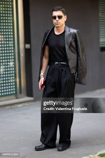 Alex Badia is seen wearing black sunglasses, a black leather jacket, a black t-shirt, black high-waist trousers and black shoes outside Magliano show...