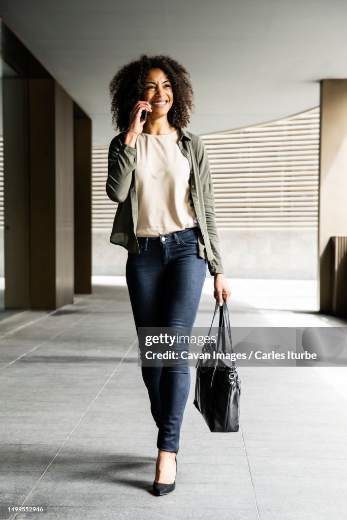 Smiling woman walking in a building using phone carrying a purse