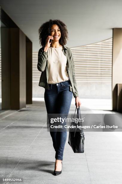 smiling woman walking in a building using phone carrying a purse - schwarze handtasche stock-fotos und bilder