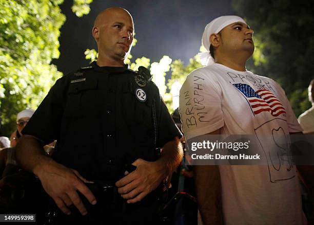 An Oak Creek police officer stands next to a Sikh American who has the name of the wounded police officer on his sleeve while attending a candle...