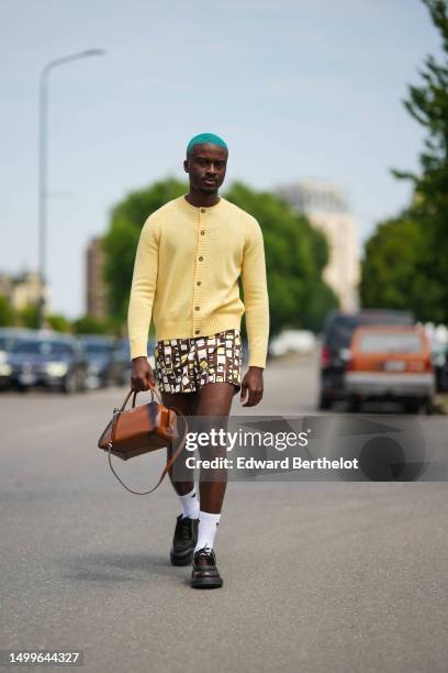 Guest wears a yellow wool buttoned cardigan, dark brown with yellow / white / black squared print pattern shorts, a camel and black tie and dye print...