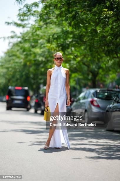 Caroline Daur wears black and orange sunglasses, a gold and diamonds pendant earrings from Tiffany, a white shirt neck / sleeveless / buttoned long...