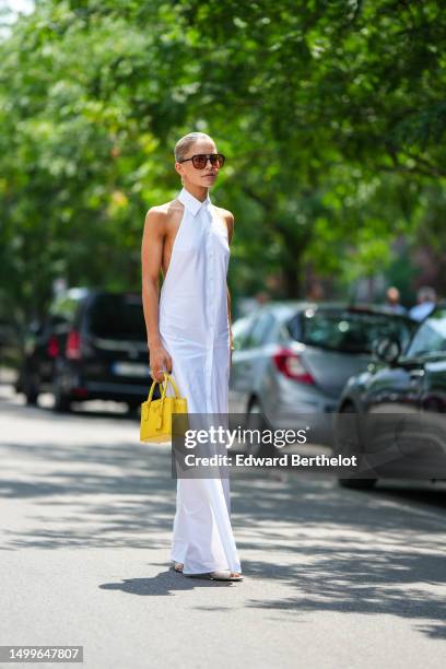 Caroline Daur wears black and orange sunglasses, a gold and diamonds pendant earrings from Tiffany, a white shirt neck / sleeveless / buttoned long...