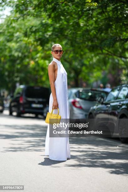Caroline Daur wears black and orange sunglasses, a gold and diamonds pendant earrings from Tiffany, a white shirt neck / sleeveless / buttoned long...