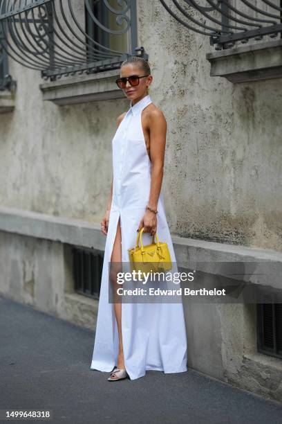 Caroline Daur wears black and orange sunglasses, a gold and diamonds pendant earrings from Tiffany, a white shirt neck / sleeveless / buttoned long...