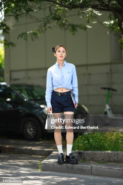 Cristine Sun wears a black silk knot hair clips, a pale blue cropped shirt from Prada, a black shiny leather large belt, navy bleu suit shorts, a...