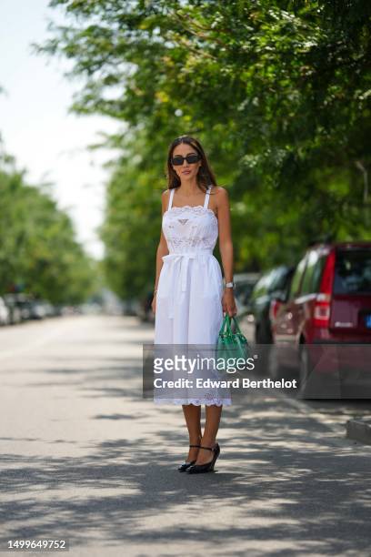 Tamara Kalinic wears black squared sunglasses from Prada, gold earrings, a white squared neck / lace embroidered pattern / tank-top / knot belt waist...
