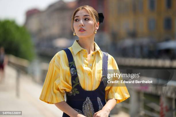 Cristine Sun wears gold earrings, a pale yellow with small white striped print pattern short sleeves shirt from Etro, a navy blue denim with...