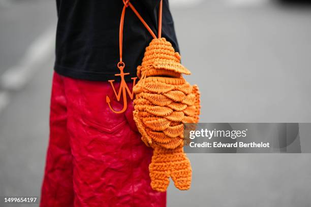 Abdulla Al Abdulla wears a black with embroidered white logo t-shirt from JW Anderson, an orange braided wool crossbody bag in shape of fish from JW...