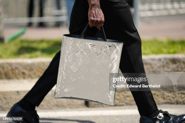 Guest wears a silver embossed striped checkered pattern metallic large tote bag from Prada, black denim pants, black shiny varnished leather shoes ,...